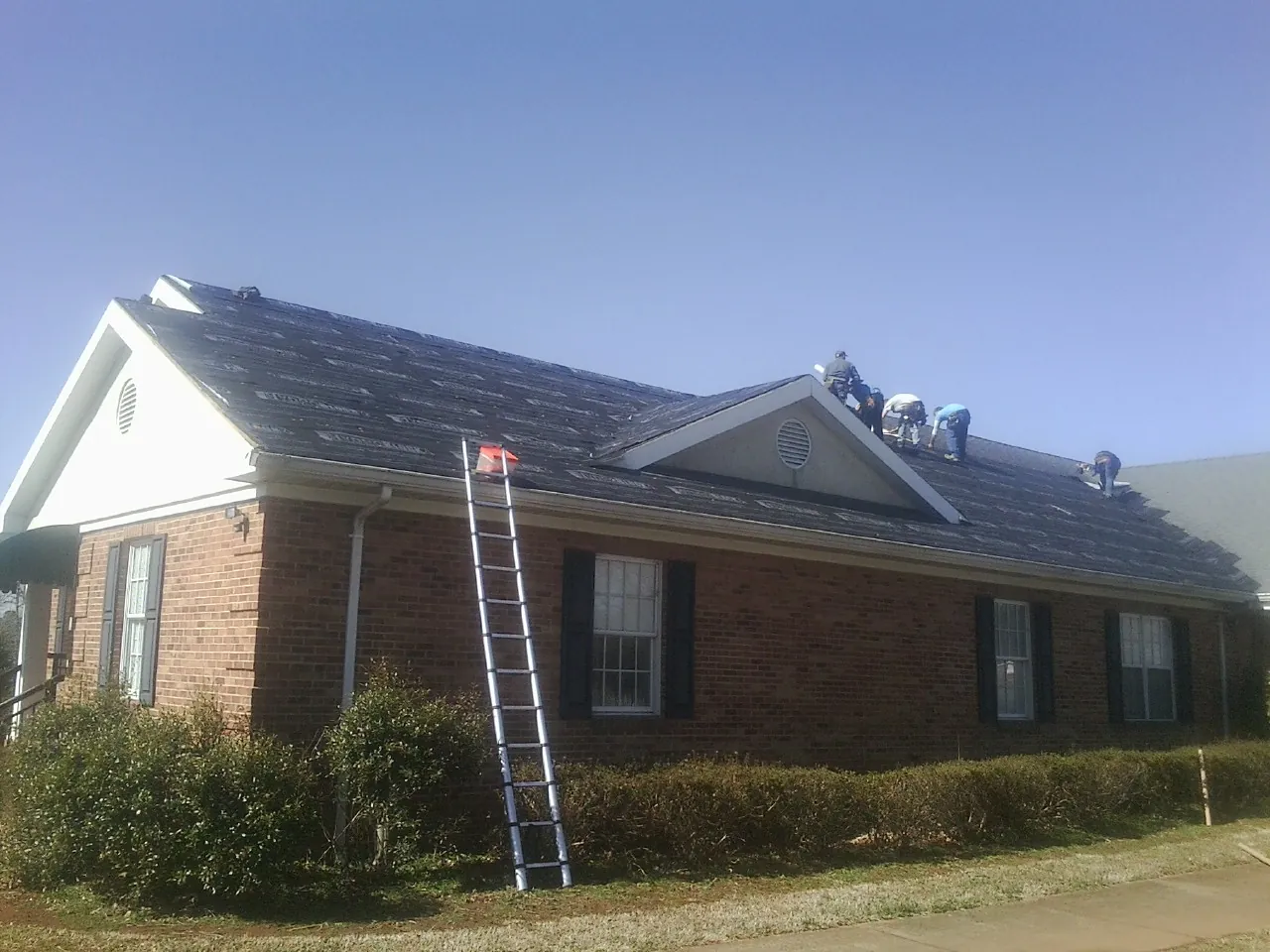 Crew tearing shingles off a brick ranch roof with a ladder set — Metal Roof Repair work by our crew in Lake Katrine