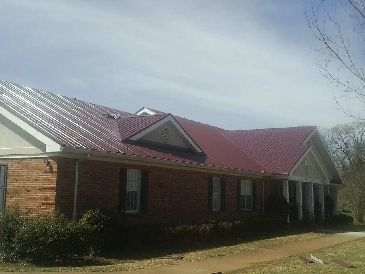 Red metal roof with gabled entries on a long brick building, from a Hail Damage Roof Repair job in Lake Katrine