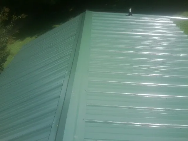 New green metal panels meeting at the ridge of a roof — Flat Roof Repair work by our crew in Lake Katrine