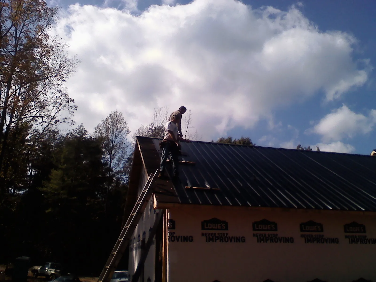 Roofer fastening dark metal panels high against a cloudy sky, from a Roof Inspection job in Lake Katrine