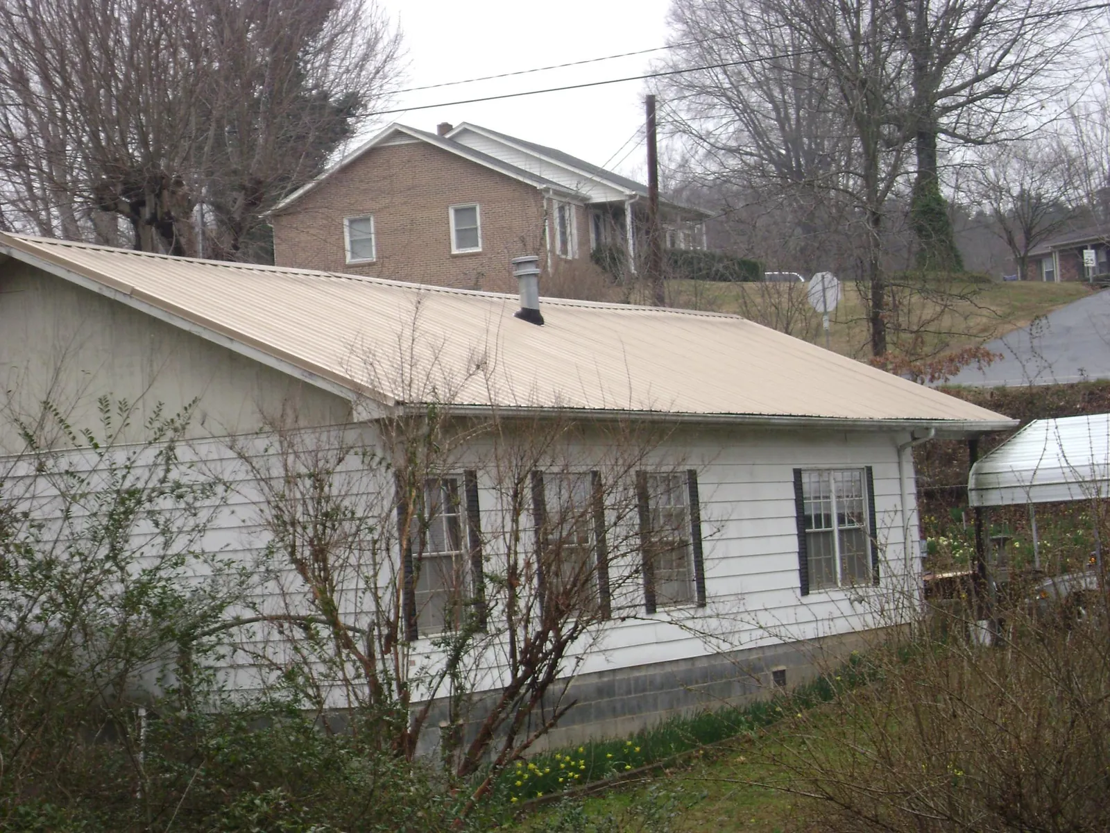 Tan metal roof on a white sided house set into a hillside — Commercial Roofing by Roofing Brothers in Lake Katrine